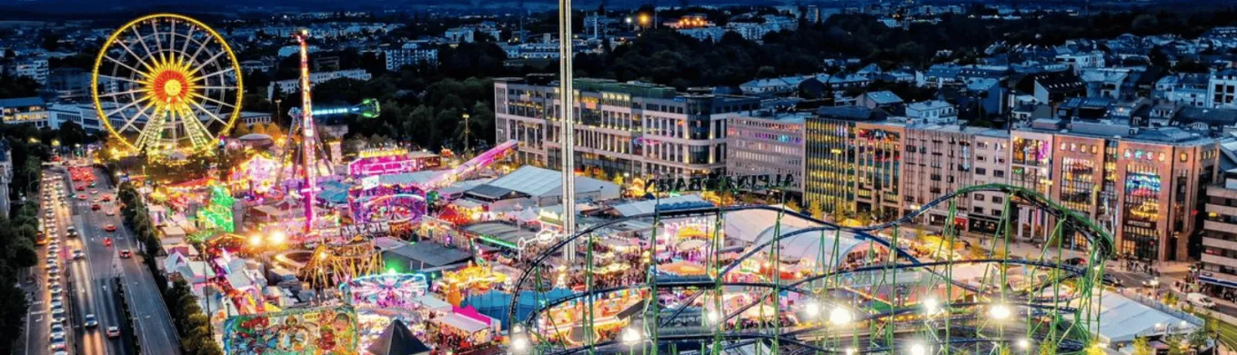 Schueberfouer Luxembourg au coucher du soleil avec grande roue illuminée, manèges et attractions: idée de sortie familiale avant la rentrée scolaire, recommandée par Pluxee Luxembourg.